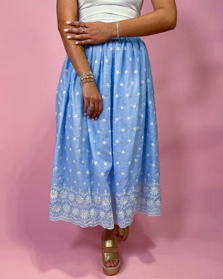 Person wearing a blue floral skirt on a pink background