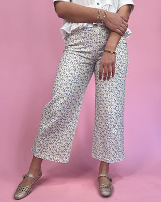 Person wearing floral pants and a white shirt on a pink background