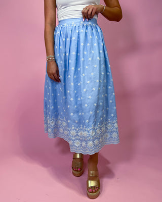 Person wearing a light blue skirt with white floral patterns on a pink background