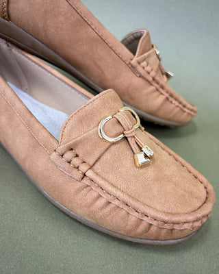 Pair of brown suede loafers with a decorative buckle on a green background