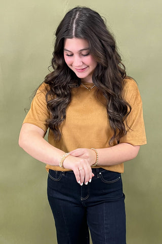 Woman wearing a mustard yellow shirt and dark jeans against a green background