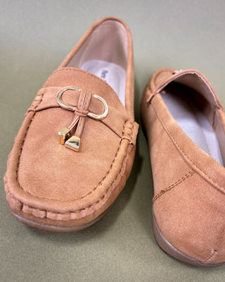 Pair of tan loafers with a decorative bow on a green background