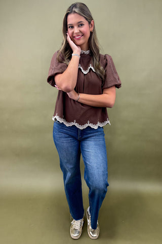 Woman wearing a brown blouse with lace trim and blue jeans against a green background