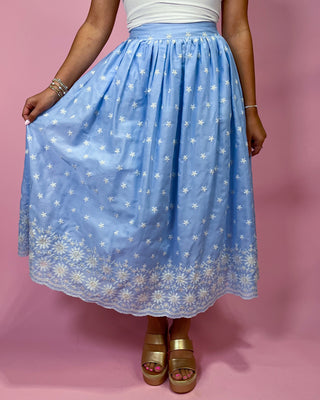 Person wearing a blue floral skirt on a pink background