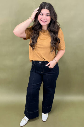 Woman wearing a mustard yellow top and dark blue jeans against a green background