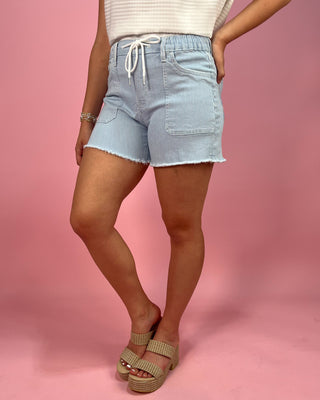 Light blue denim shorts worn by a person on a pink background