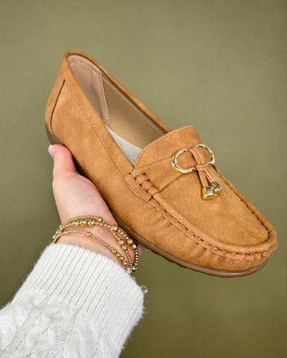 Tan loafer shoe held by a hand against a green background