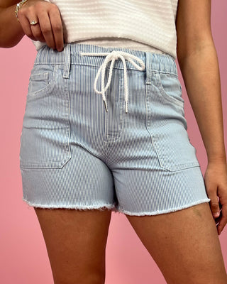 Light blue striped shorts worn by a person on a pink background