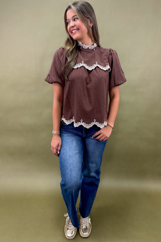 Woman wearing a brown blouse with lace details and blue jeans on a green background