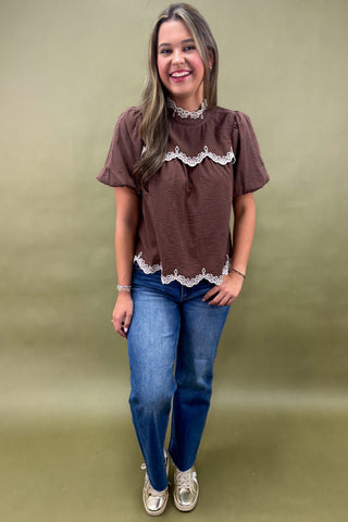 Woman wearing a brown blouse with lace details and blue jeans on a green background