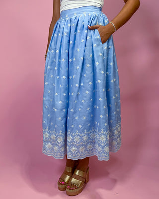 Person wearing a blue floral skirt against a pink background