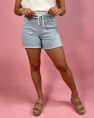 Person wearing light blue denim shorts on a pink background