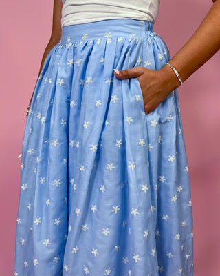 Person wearing a blue floral skirt with a pink background