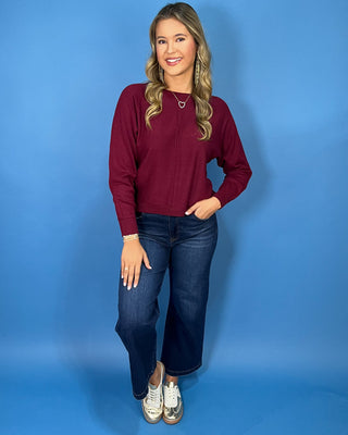 Burgundy long sleeve knit sweater with a round neckline, center seam detail, ribbed cuffs and hem, and relaxed fit.