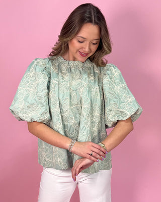 Woman wearing a light green blouse with white patterns against a pink background