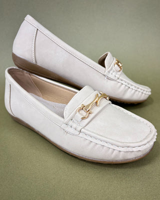 Pair of white loafers with gold accents on a green background