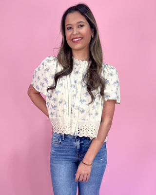 Woman wearing a floral blouse and blue jeans against a pink background