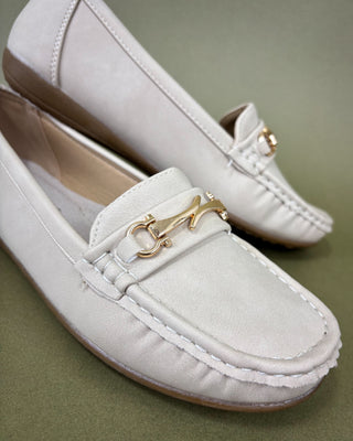 White loafers with gold accents on a green background