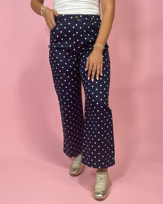 Navy blue pants with white polka dots worn by a person on a pink background