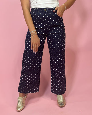 Person wearing navy blue pants with white polka dots on a pink background