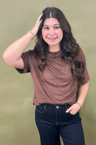 Woman wearing a brown shirt and dark jeans against a green background