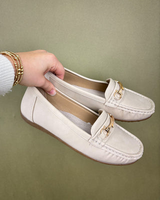 White loafers with gold accents held by a hand against a green background