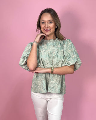 Woman wearing a green patterned blouse against a pink background