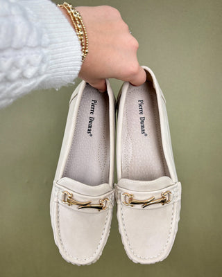 White loafers with gold accents held by a person against a green background