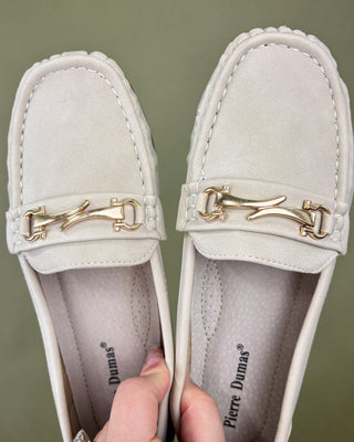 White loafers with gold accents held by a hand against a green background
