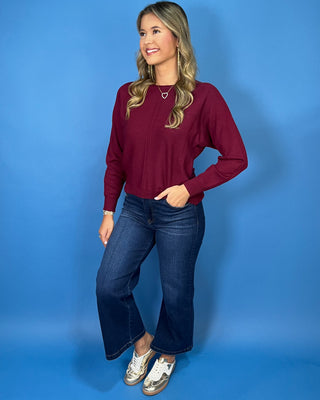 Burgundy long sleeve knit sweater with a round neckline, center seam detail, ribbed cuffs and hem, and relaxed fit.