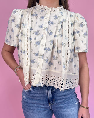 Person wearing a floral blouse with lace details against a pink background