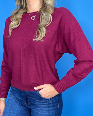 Burgundy long sleeve knit sweater with a round neckline, center seam detail, ribbed cuffs and hem, and relaxed fit.