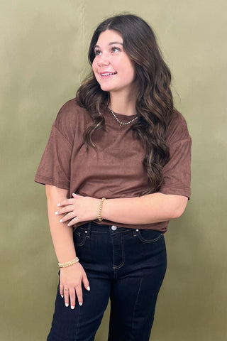 Woman wearing a brown t-shirt and dark jeans against a green background