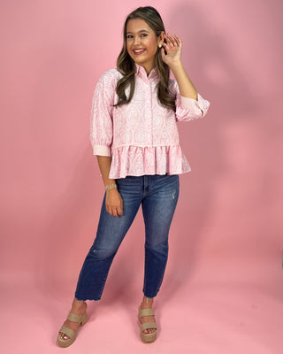 Woman wearing a pink patterned blouse and blue jeans against a pink background