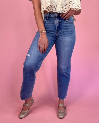 Person wearing blue jeans and a white lace top on a pink background