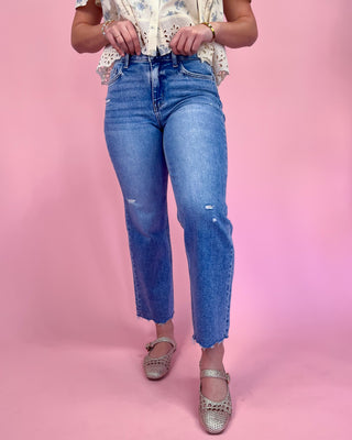 Person wearing blue jeans and a patterned top on a pink background