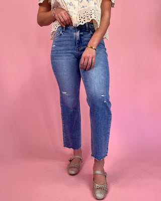 Person wearing blue jeans and a white top with lace details on a pink background