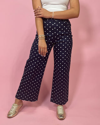 Person wearing navy blue pants with white polka dots on a pink background
