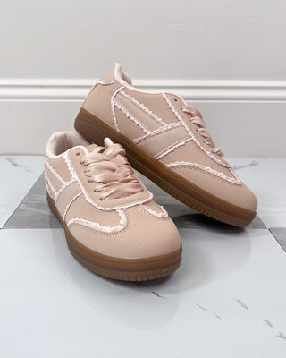 Pair of beige sneakers with brown soles on a light gray surface.