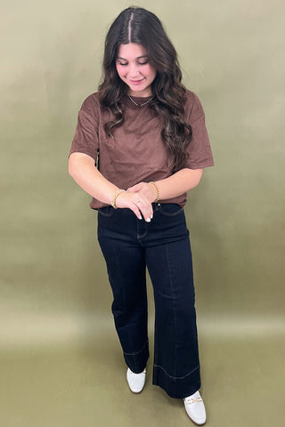 Woman wearing a brown t-shirt and dark jeans against a green background