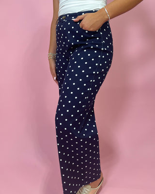 Navy blue pants with white polka dots worn by a person on a pink background