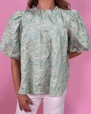 Light green blouse with floral patterns worn by a person on a pink background