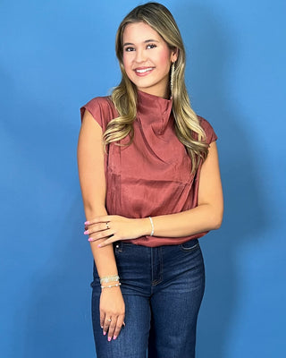 Rust satin sleeveless top with draped mock neckline, structured shoulders, and relaxed fit.