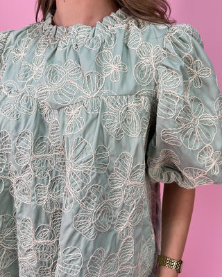 Light blue dress with white floral embroidery on a pink background