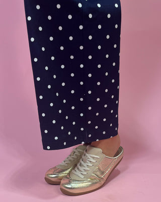 Navy pants with white polka dots and gold sneakers on a pink background