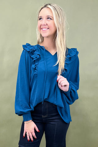 Woman wearing a blue blouse with ruffled sleeves against a green background
