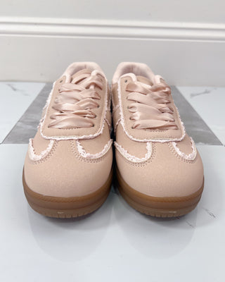 Pair of pink sneakers with brown soles on a white and gray striped surface.