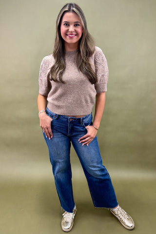 Woman wearing a beige sweater and blue jeans against a green background