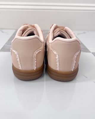 Pair of beige sneakers with brown soles on a white surface