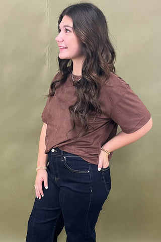 Woman wearing a brown shirt and dark jeans against a green background